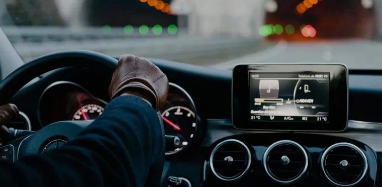 A chauffeur's gloved hands on the wheel of a Mercedes, city lights ahead