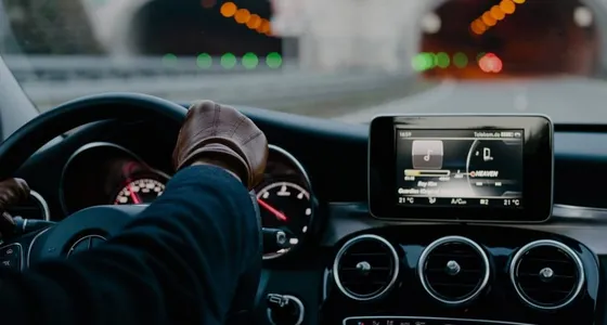 A chauffeur's gloved hands on the wheel of a Mercedes, city lights ahead