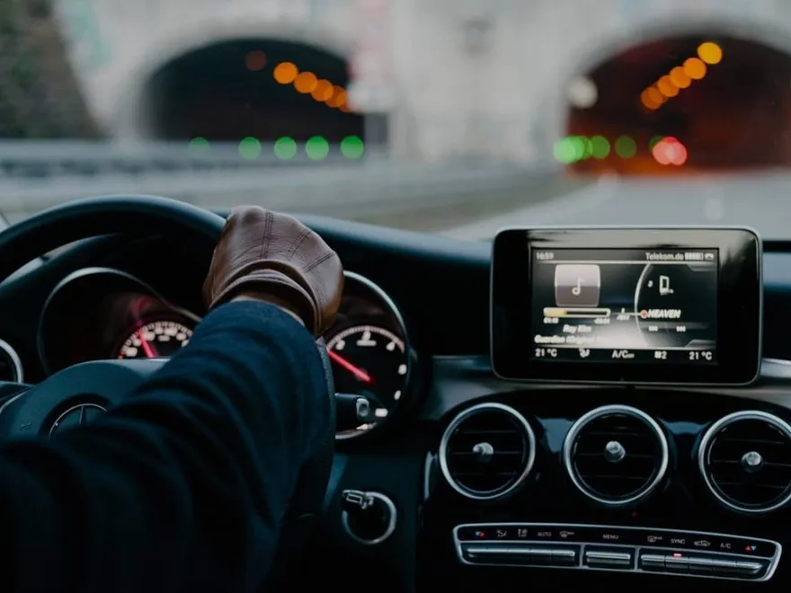 A chauffeur's gloved hands on the wheel of a Mercedes, city lights ahead