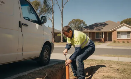 An Australian plumber in uniform working on site beside a signed work van