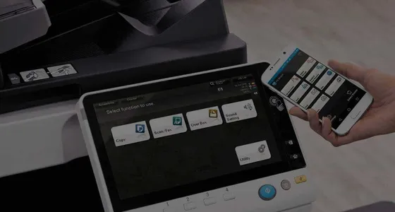 A hand operating the touchscreen on a Konica Minolta multifunction printer