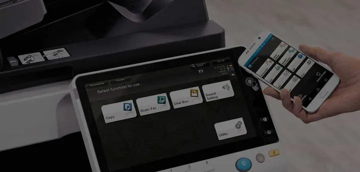 A hand operating the touchscreen on a Konica Minolta multifunction printer