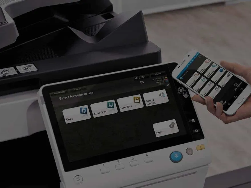 A hand operating the touchscreen on a Konica Minolta multifunction printer
