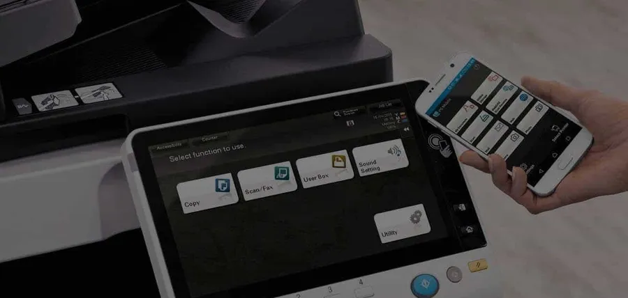 A hand operating the touchscreen on a Konica Minolta multifunction printer