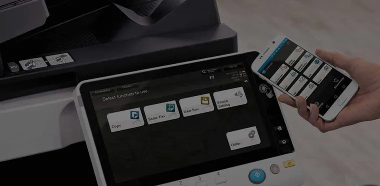 A hand operating the touchscreen on a Konica Minolta multifunction printer
